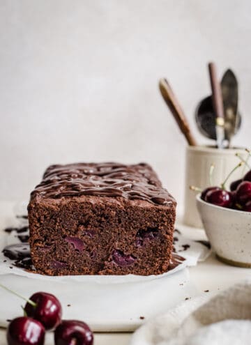 chocolate cherry cake on a cake board next to a bowl of cherries