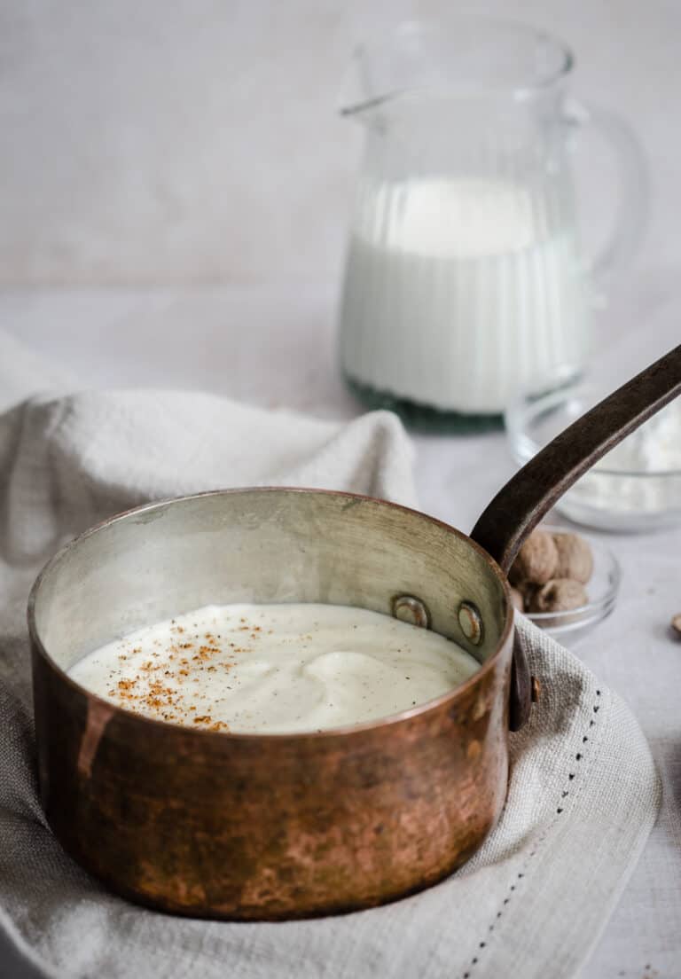white sauce in a saucepan surrounded by ingredients