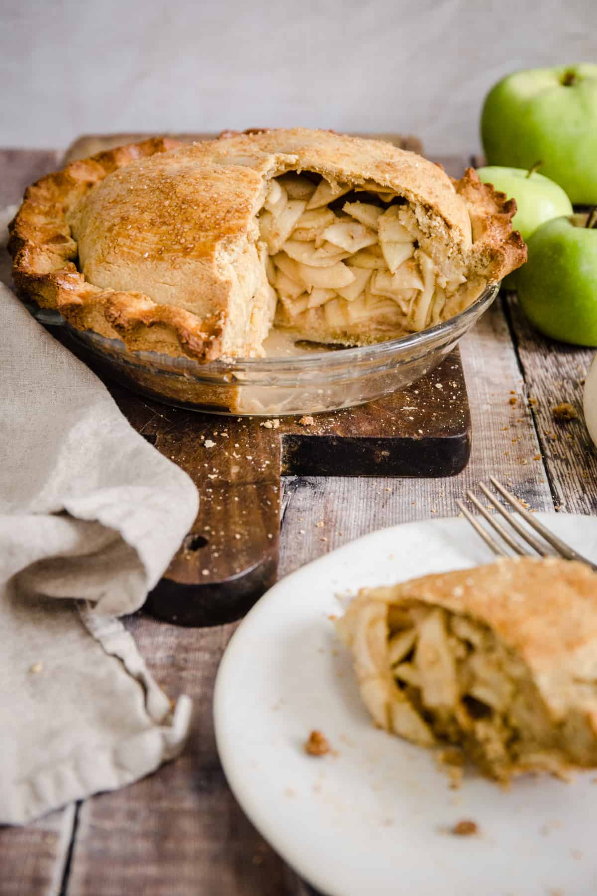 Cut open apple pie on a wooden board next to apples