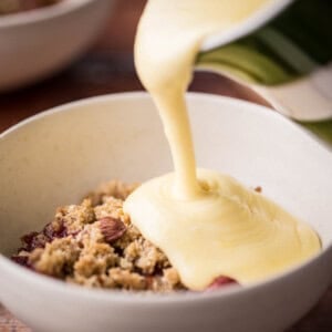 custard pouring from jug into a bowl of dessert next to spoons
