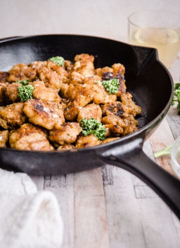 Gluten-Free Fried Popcorn Chicken in a cast iron skillet on table next to sauce and parsley