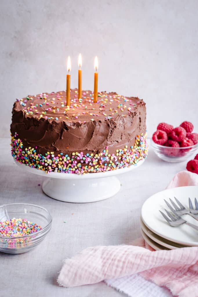 Birthday cake on a stand with raspberries and sprinkles around