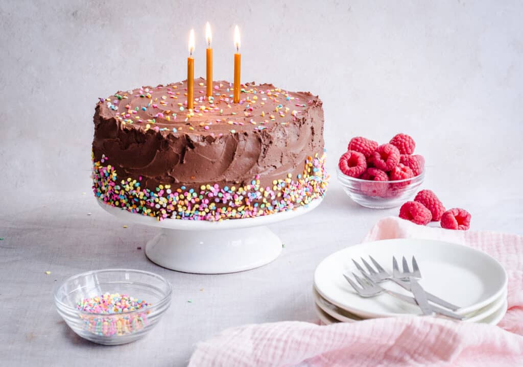 Birthday cake on a stand with raspberries and sprinkles around
