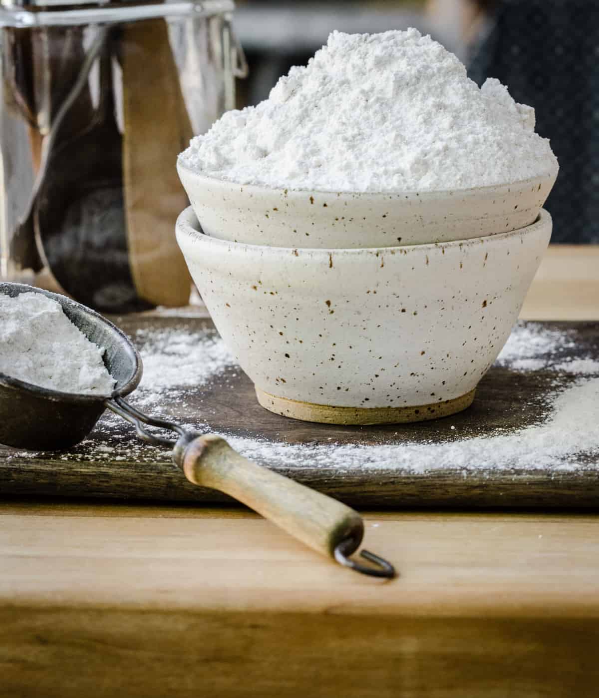 flour in a bowl on a wooden board next to scoop