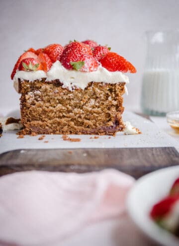 Cut Strawberry Honey Cake on a board next to cloth, strawberries and milk