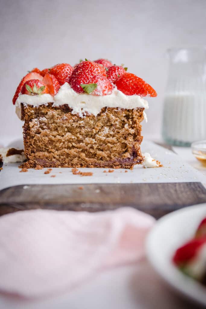 Cut Strawberry Honey Cake on a board next to cloth, strawberries and milk