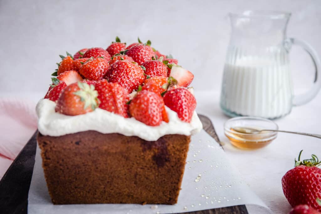 Strawberry Honey Cake on a board next to cloth, strawberries and milk