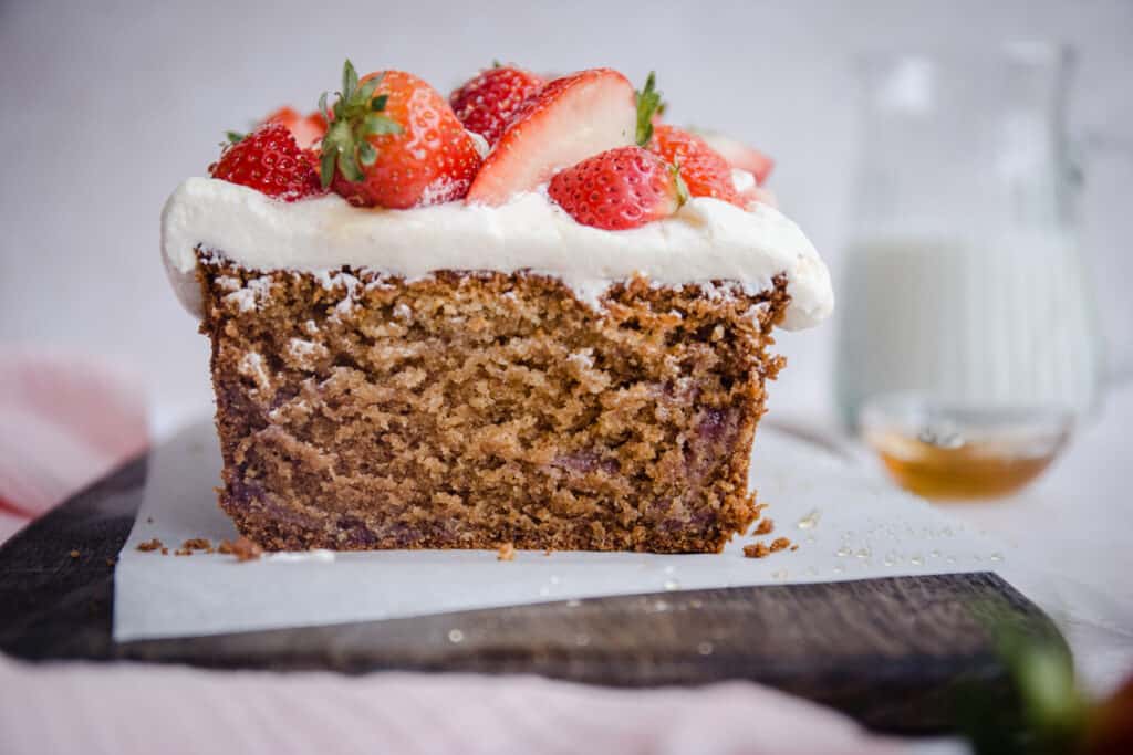 Cut Strawberry Honey Cake on a board next to cloth, strawberries and milk