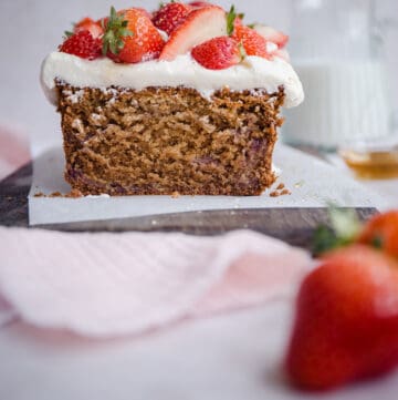 Cut Strawberry Honey Cake on a board next to cloth, strawberries and milk