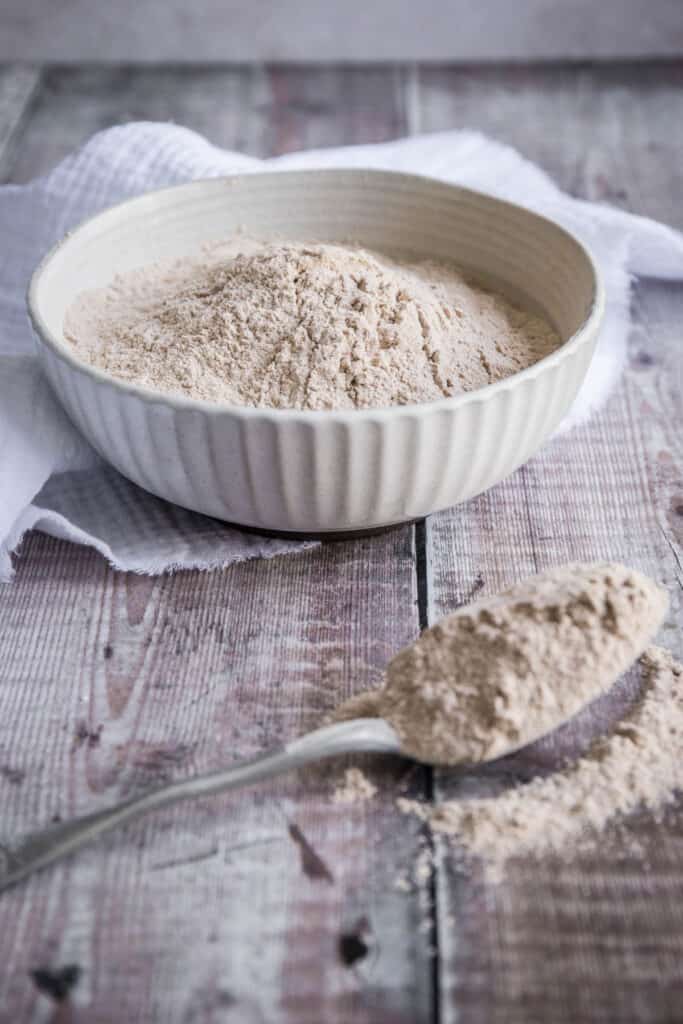 spoon of green banana flour in front of a bowl of flour