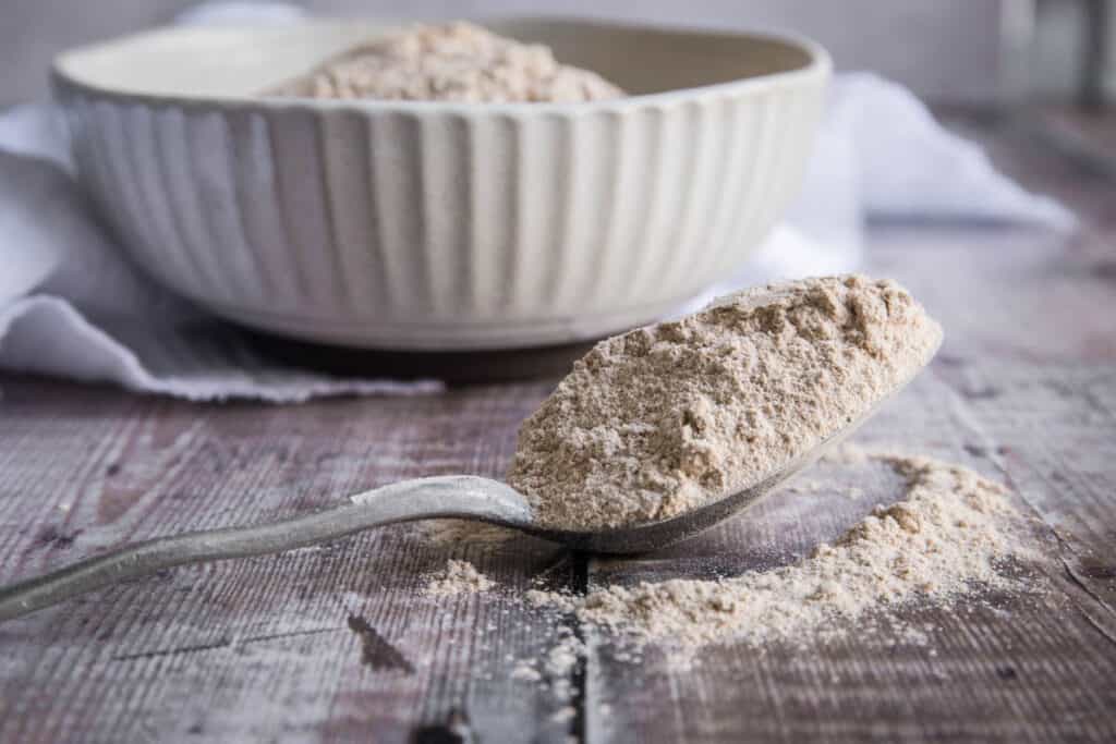 spoon of green banana flour in front of a bowl