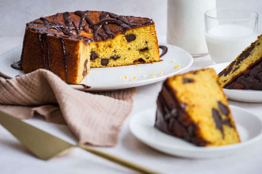 orange cake with chocolate chips on a plate with slice taken out and slice of cake on a plate in front