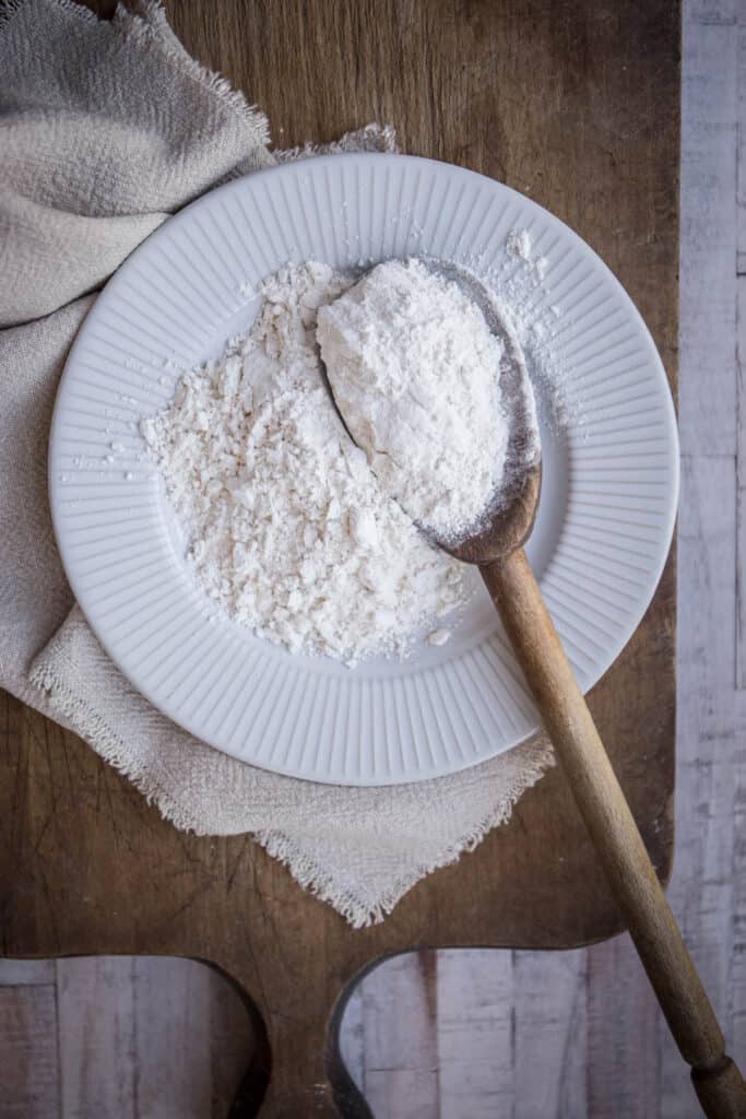 cassava flour on a plate with a wooden spoon. cloth and wooden board behind.