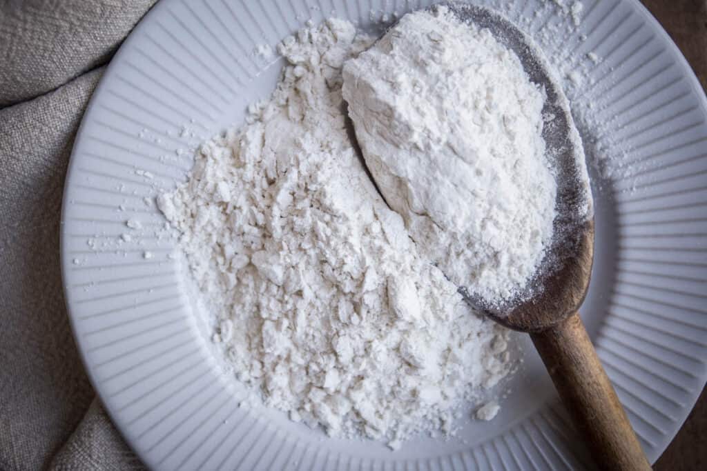 cassava flour on a plate with a wooden spoon. cloth and wooden board behind.