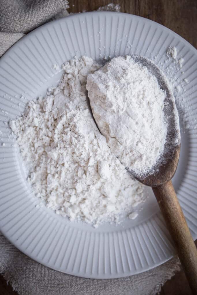 cassava flour on a plate with a wooden spoon. cloth and wooden board behind.