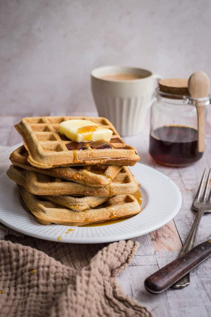 Gluten-free waffles stacked on a plate on a table next to cutlery