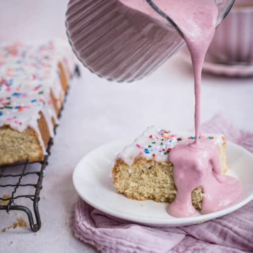 strawberry custard poured from a jug over plate of cake