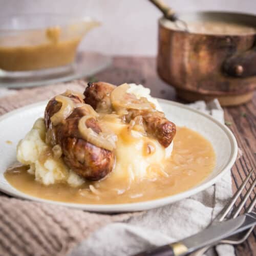onion gravy over a plate of sausage and mash, surrounded by gravy boat and saucepan
