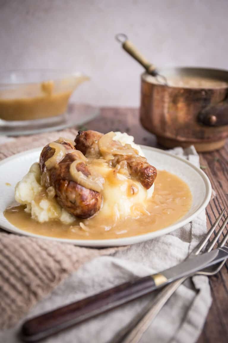 onion gravy over a plate of sausage and mash, surrounded by gravy boat and saucepan