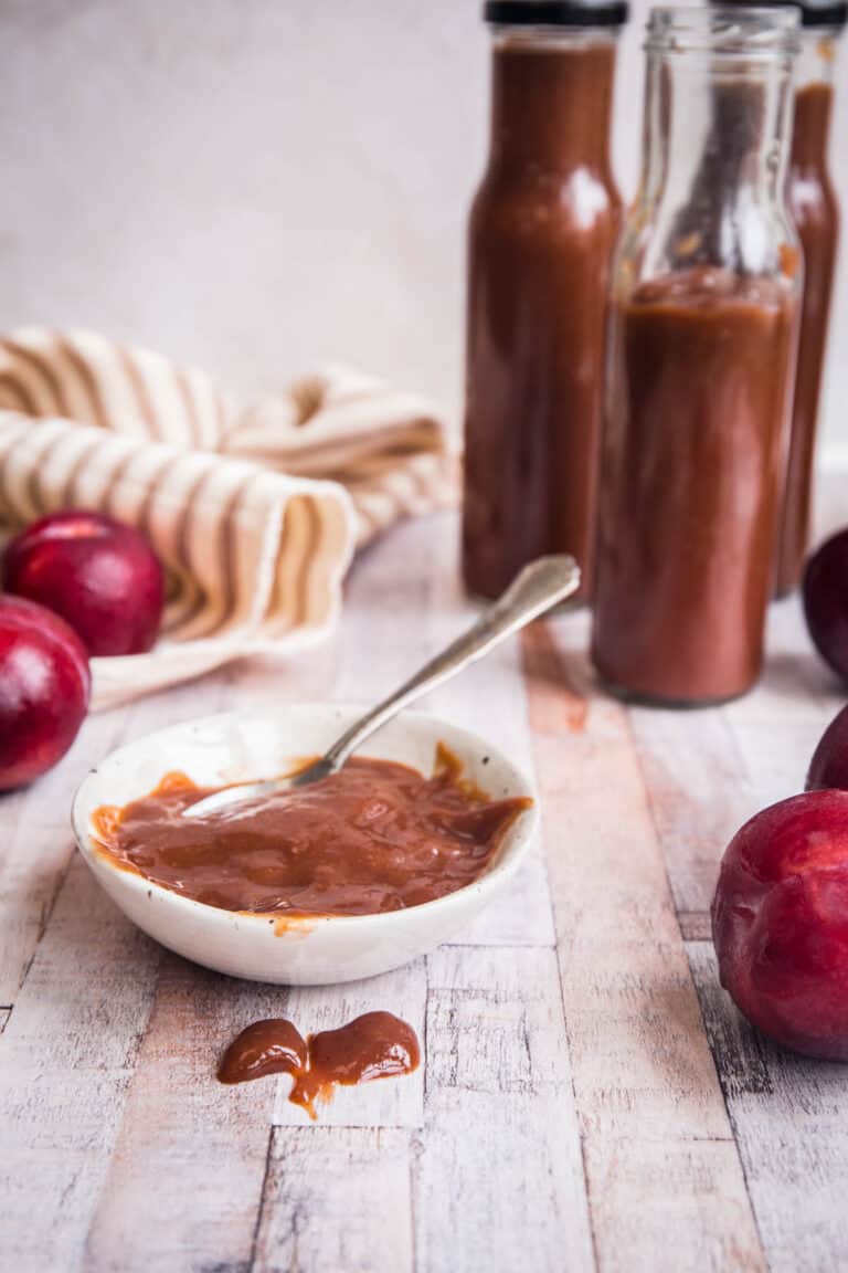 close up of bbq sauce in a pot next to plums and bottles of sauce