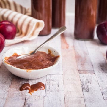 close up of bbq sauce in a pot next to plums and open bottle of sauce