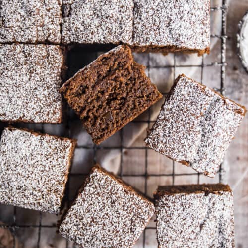 cross section of a piece of sticky gingerbread cake next to all the pieces of cake on a wire rack