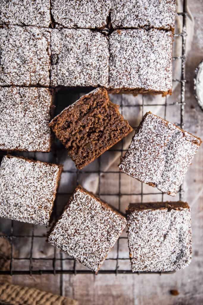 cross section of a piece of sticky gingerbread cake next to all the pieces of cake on a wire rack