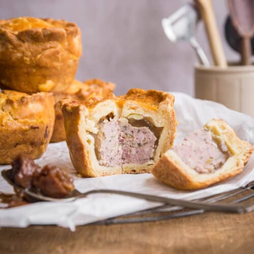 Cut open pork pie next to chutney and pile of pies