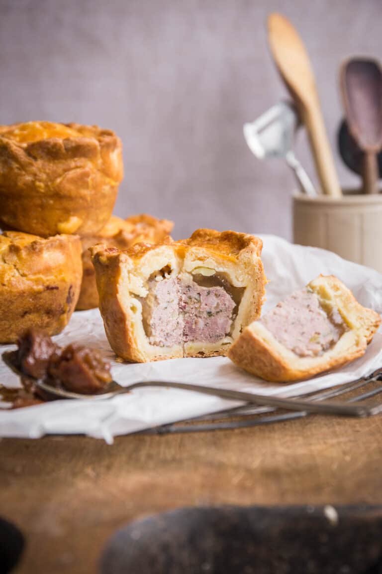 Cut open pork pie next to chutney and pile of pies
