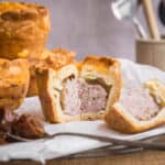 Cut open pork pie next to chutney and pile of pies