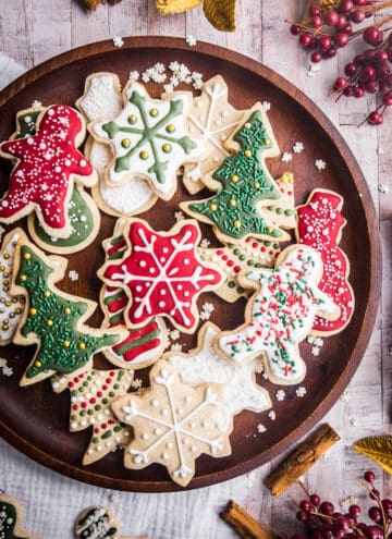 Wooden plate full of Christmas Cookies with Christmas Decorations surrounding