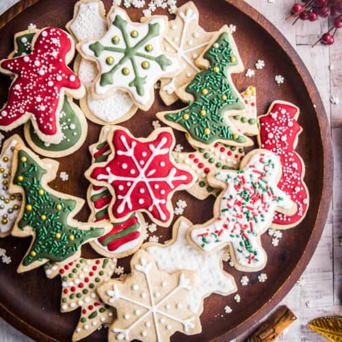 Wooden plate full of Christmas Cookies with Christmas Decorations surrounding