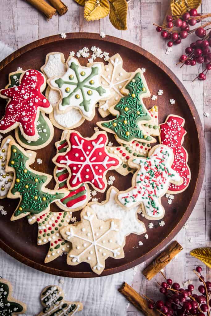 Wooden plate full of Christmas Cookies with Christmas Decorations surrounding