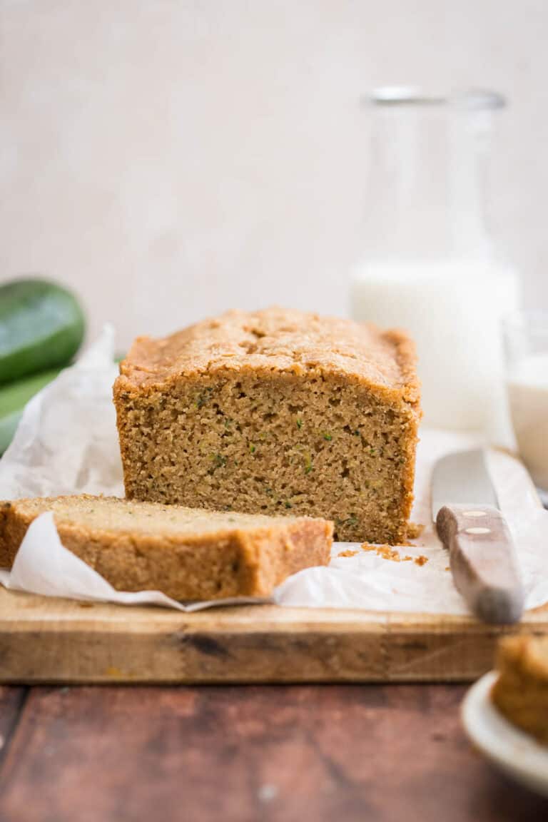 Gluten Free Zucchini Bread on wooden board , sliced. Next to knife, courgette and milk.