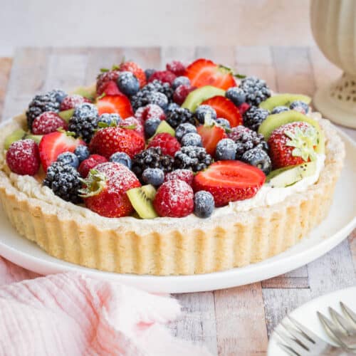 Gluten-Free Fruit Tart on a plate next to pink napkin, plates, forks and teapot and cup
