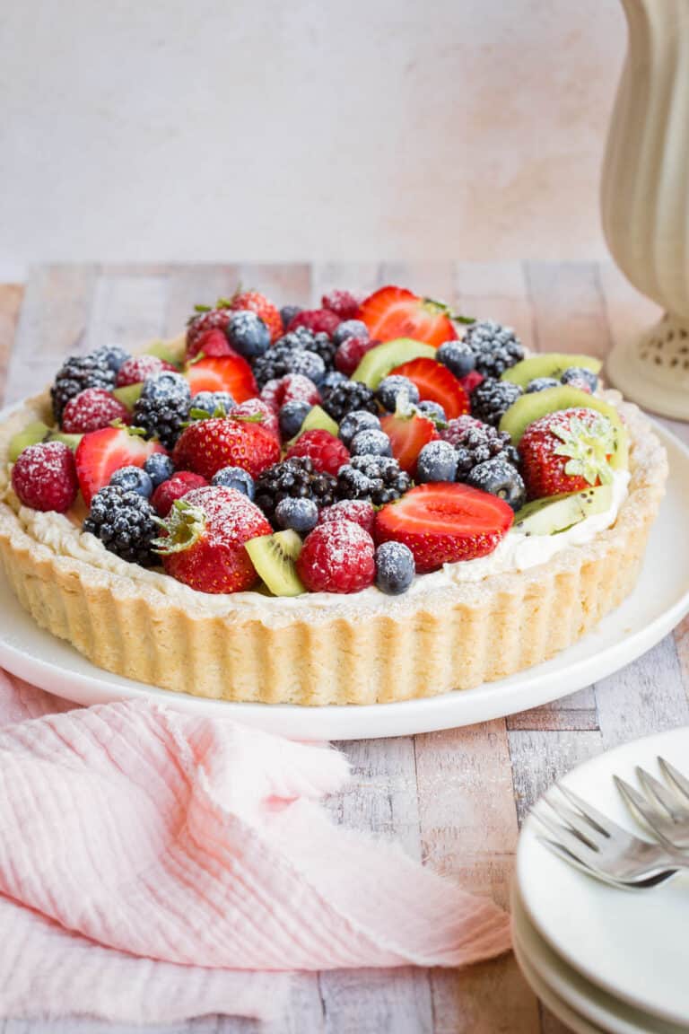 Gluten-Free Fruit Tart on a plate next to pink napkin, plates, forks and teapot and cup