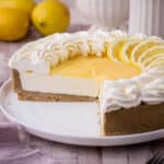 Lemon Curd Cheesecake on a plate with slices cut from it. Lemons behind.