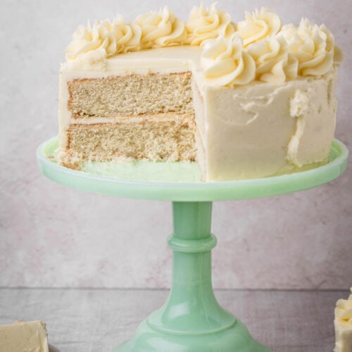 Gluten-Free Vanilla Cake on a cake stand surrounded by cakes on plates.