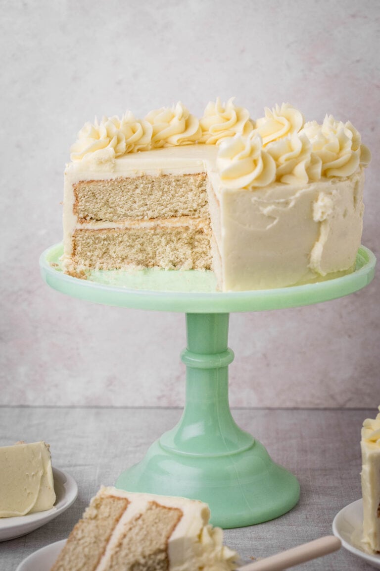 Gluten-Free Vanilla Cake on a cake stand surrounded by cakes on plates.