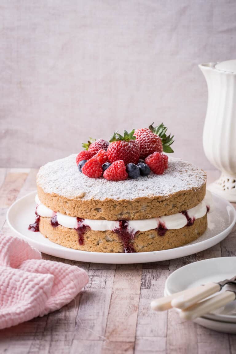 Gluten-Free Vegan Vanilla Cake on Cake plate with fresh fruit piled on top.