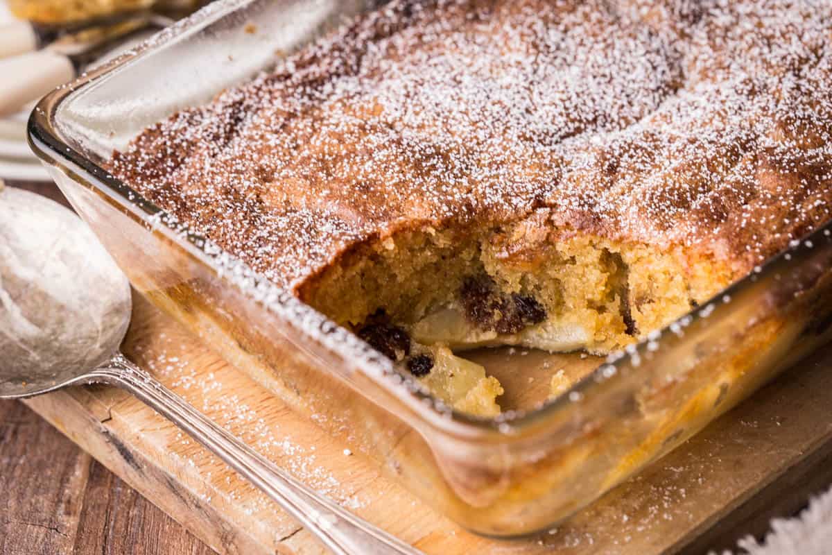 Large baking dish of Bramley Apple Mincemeat Pudding with portion spooned out showing light and fluffy sponge.