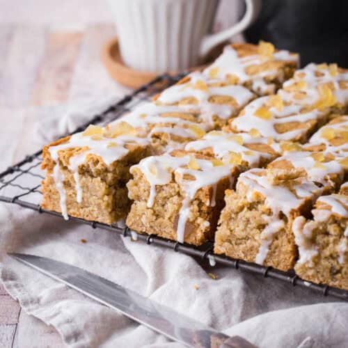 A cooling rack full of lemon iced ginger parkin next to a steaming hot cup of tea.