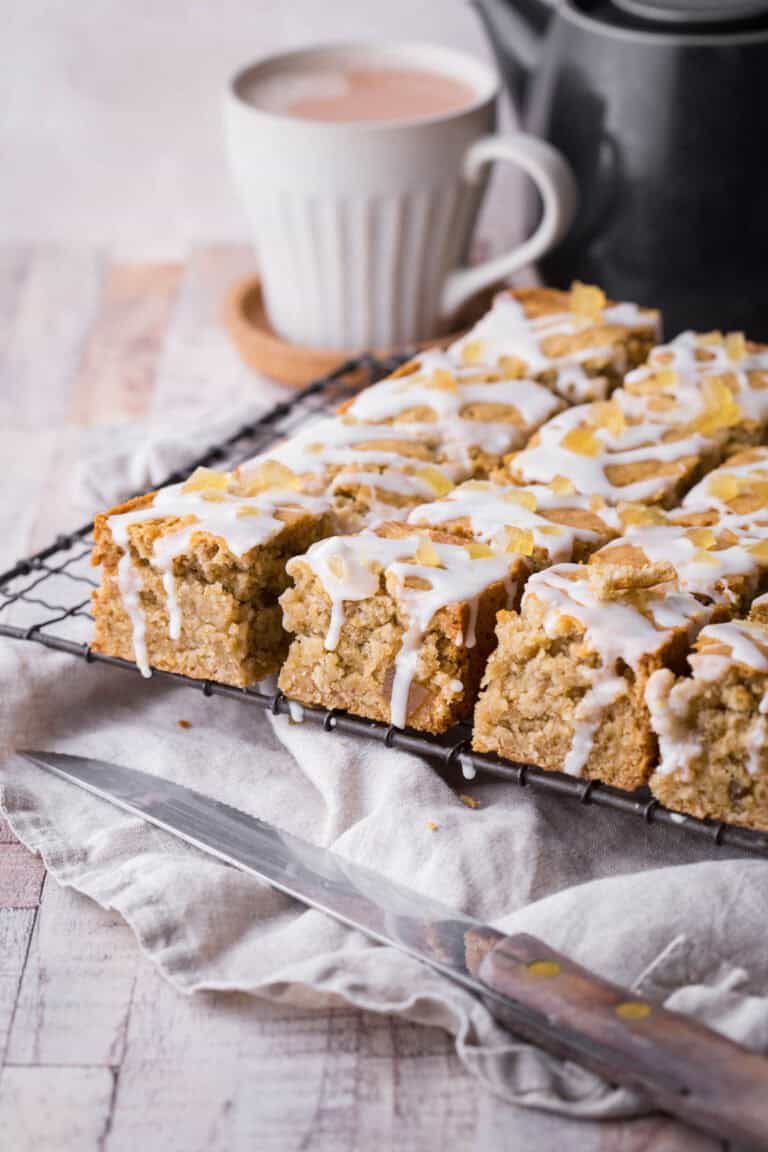 A cooling rack full of lemon iced ginger parkin next to a steaming hot cup of tea.