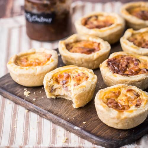 Mini Quiche on a wooden board. One with bite taken out showing meaty creamy inside.