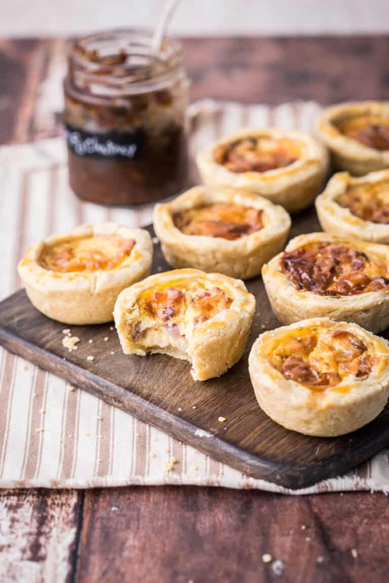 Mini Quiche on a wooden board. One with bite taken out showing meaty creamy inside.