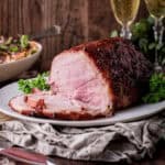A whole Christmas Ham sliced on a plate showing tender succulent meat inside with crisp glazed surface.