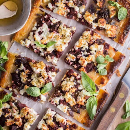 Sliced Gluten Free Puff Pastry Feta Beetroot Tart on a board surrounded by fresh herbs.