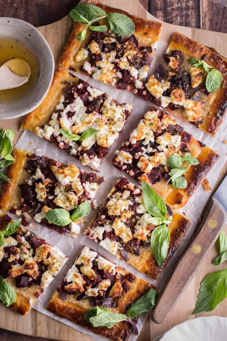 Sliced Gluten Free Puff Pastry Feta Beetroot Tart on a board surrounded by fresh herbs.