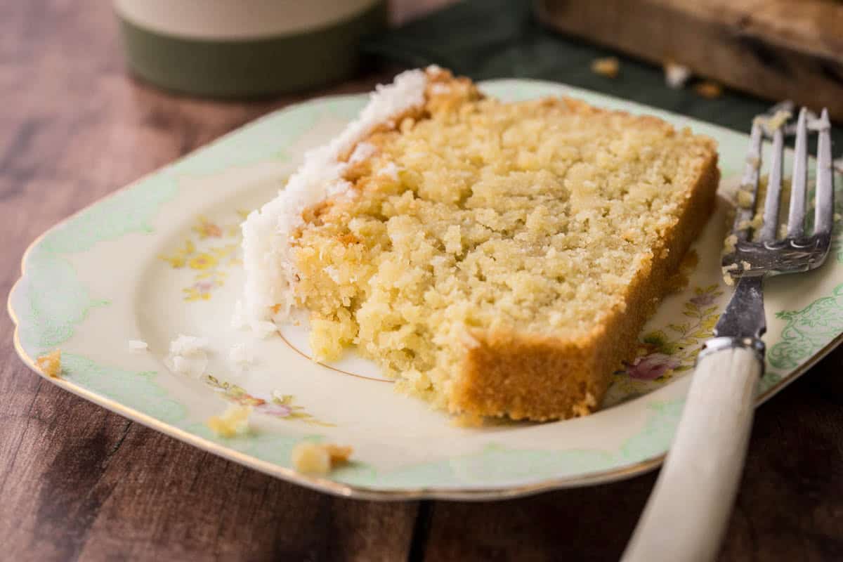 Slice of Gluten-Free Lime and Coconut Loaf Cake on a plate with a fork showing soft and tender texture.
