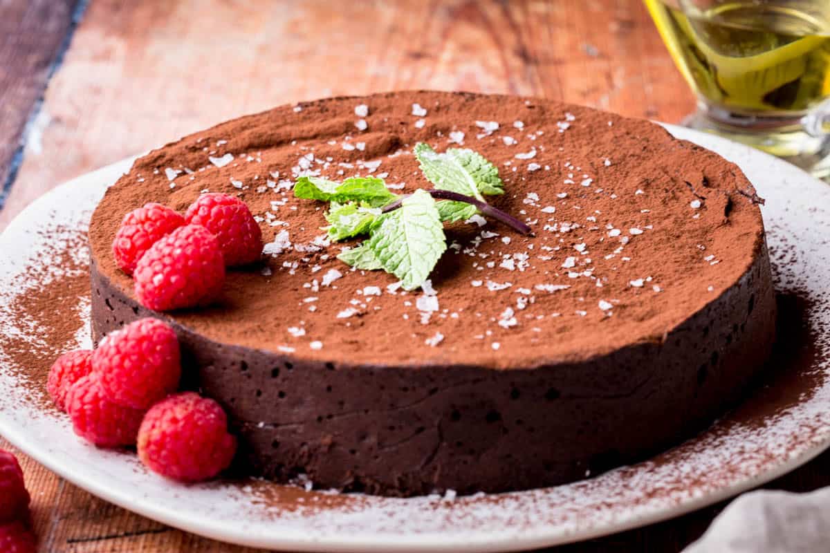 Flourless Olive Oil Chocolate Cake dusted with cocoa powder, sprinkled with flaky sea salt and decorated with a mint leaf and raspberries.